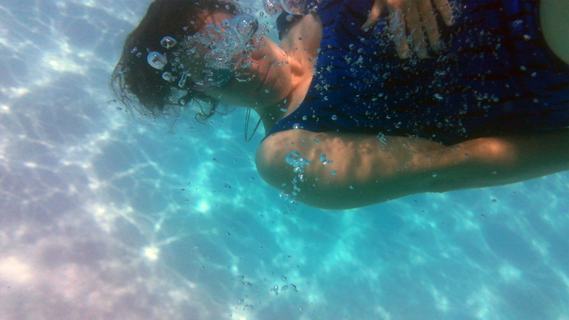 a person hovering in water face obscured by air bubbles, a hand on her torso